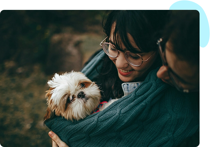 A smiling woman holding a small shih tzu wrapped in her sweater