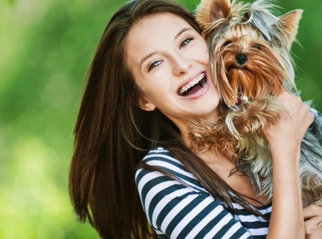 A laughing young woman hugging her Yorkshire terrier outdoors